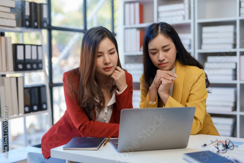 Two happy asian businesswoman talking and using a laptop computer in a meeting.