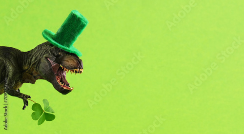 Green dinosaur in green hat holds leaf of clover. Wide banner. Copy space. photo