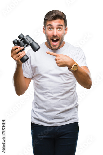 Young handsome man looking through binoculars over isolated background very happy pointing with hand and finger