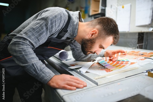 Print house worker controlling printing process quality and checking colors with magnifying glass photo