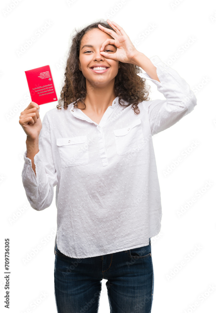 Young hispanic woman holding passport of Switzerland with happy face smiling doing ok sign with hand on eye looking through fingers Young hispanic woman holding passport of Switzerland with happy face smiling doing ok sign with hand on eye looking through fingers