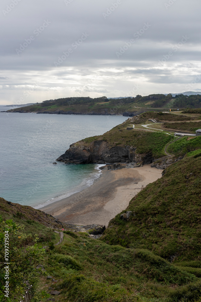 a scenic view of a secluded beach, surrounded by greenery and cliffs, under a cloudy sky