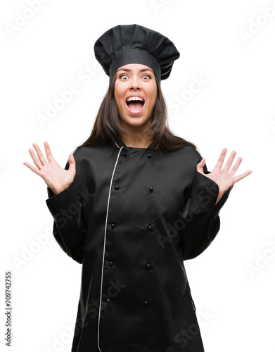 Young hispanic cook woman wearing chef uniform very happy and excited, winner expression celebrating victory screaming with big smile and raised hands