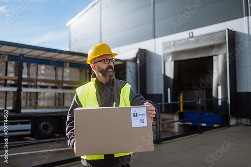 Warehouse receiver unloading truck in front of warehouse, carrying cardboard box with delivered items. photo