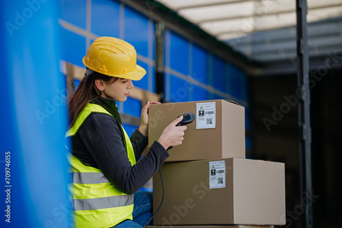 Warehouse receiver kneeling inside of truck in cargo area, trailer, barcode scanning delivered items. Receiving clerk holding scanner checking delivered goods against order.