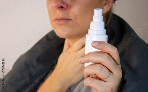 Sick woman holding a spray for soar throat, sitting on sofa with blanket