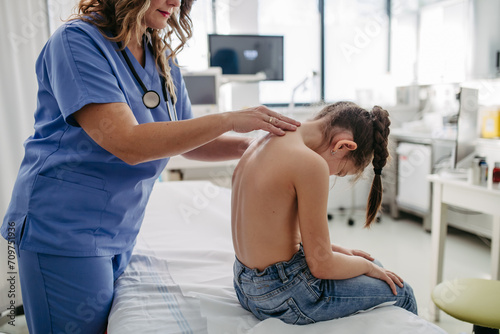 Orthopedist examines the spine, posture, and spinal deformities of little girl. Girl visiting paediatrician for annual preventive exam. Concept of preventive health care for children. photo