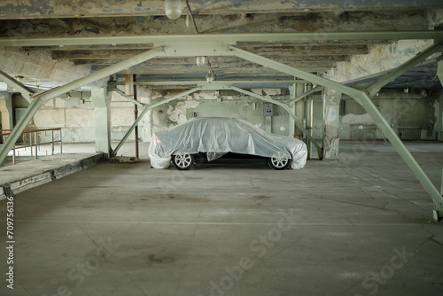 Car covered with a protective film in an abandoned car park. Selective focus.