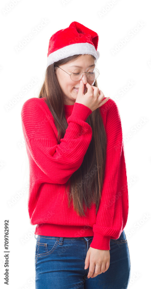 Young Chinese woman over isolated background wearing christmas hat smelling something stinky and disgusting, intolerable smell, holding breath with fingers on nose. Bad smells concept. Young Chinese woman over isolated background wearing christmas hat smelling something stinky and disgusting, intolerable smell, holding breath with fingers on nose. Bad smells concept.
