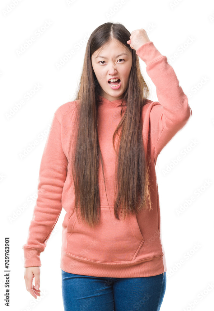 Young Chinese woman over isolated background wearing sport sweathshirt angry and mad raising fist frustrated and furious while shouting with anger. Rage and aggressive concept. Young Chinese woman over isolated background wearing sport sweathshirt angry and mad raising fist frustrated and furious while shouting with anger. Rage and aggressive concept.