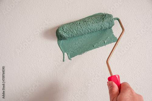 Repairman painting white wall in apartment green using roller, closeup