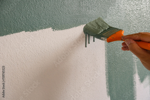 Repairman painting white wall in apartment green using brush, closeup