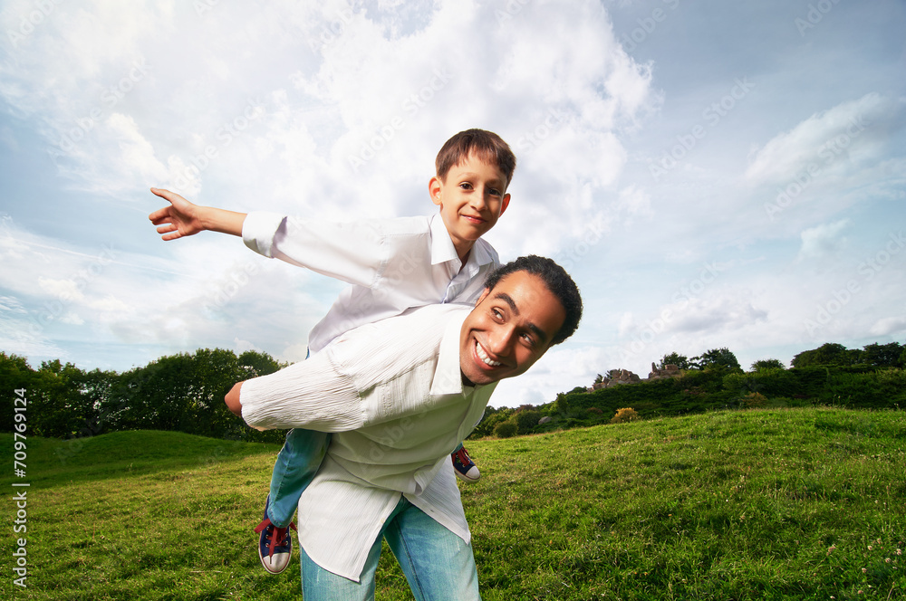 Man giving young boy piggyback ride outdoors smiling in the park. Man giving young boy piggyback ride outdoors smiling in the park.