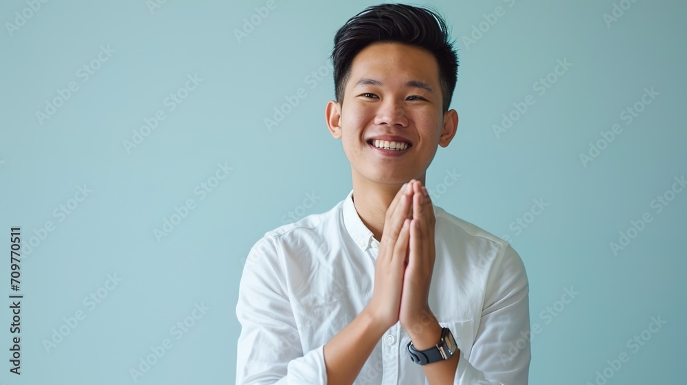 Young, attractive, smiling man from Southeast Asia clapping hands against a blue backdrop - obrazy, fototapety, plakaty 