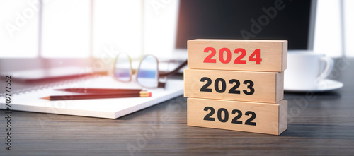 3D render of a stacked wooden blocks with year number 2022 2023 2024 on a office workplace background - 3D illustration