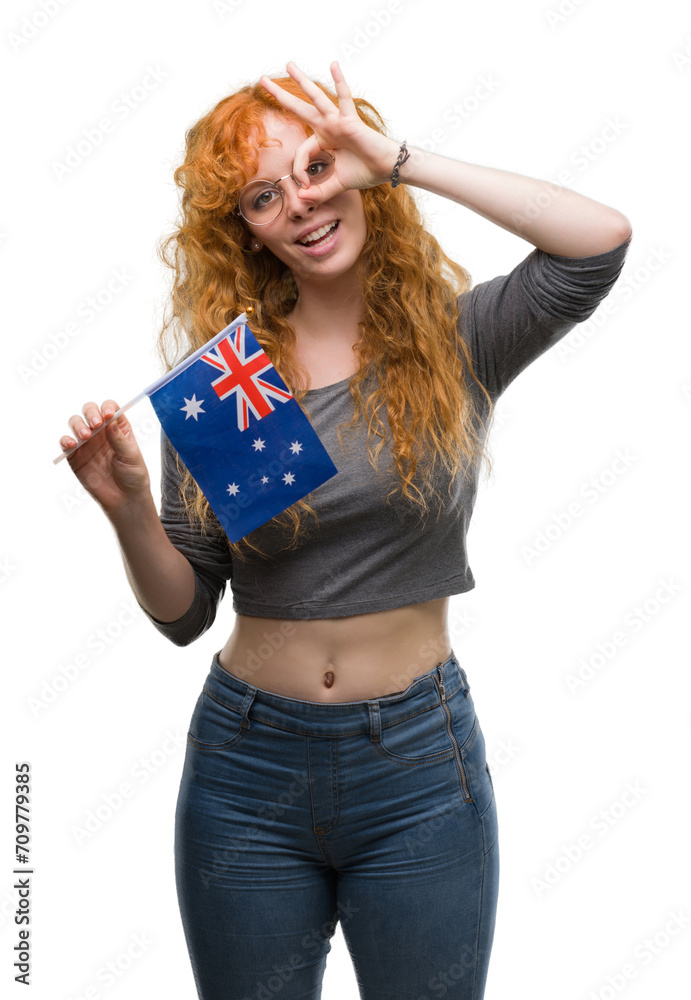 Young redhead woman holding flag of Australia with happy face smiling doing ok sign with hand on eye looking through fingers Young redhead woman holding flag of Australia with happy face smiling doing ok sign with hand on eye looking through fingers