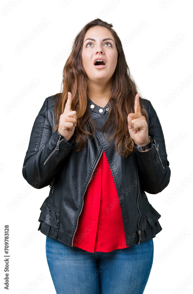 Beautiful plus size young woman wearing a fashion leather jacket over isolated background amazed and surprised looking up and pointing with fingers and raised arms. Beautiful plus size young woman wearing a fashion leather jacket over isolated background amazed and surprised looking up and pointing with fingers and raised arms.