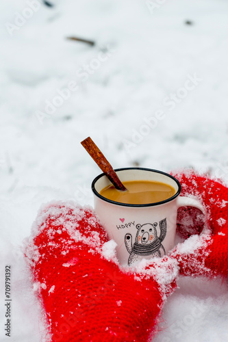 The girl's hands in red knitted mittens hold a cup of hot aromatic cocoa. Warmth, comfort, winter atmosphere, snow, nature. Winter hot drink with cinnamon and spices.