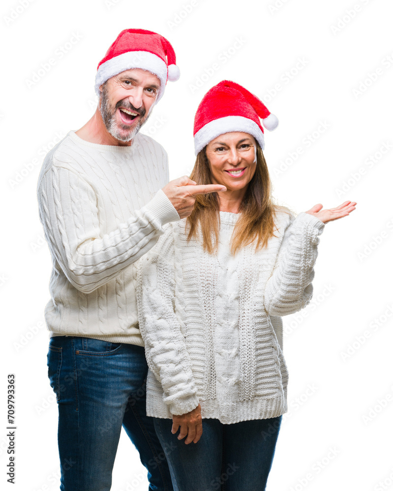 Middle age hispanic couple wearing christmas hat over isolated background amazed and smiling to the camera while presenting with hand and pointing with finger. Middle age hispanic couple wearing christmas hat over isolated background amazed and smiling to the camera while presenting with hand and pointing with finger.