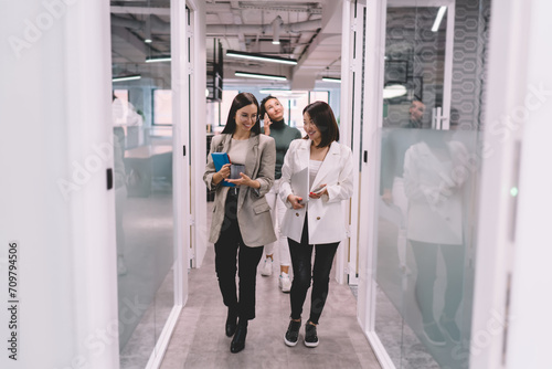 Cheerful diverse coworkers walking in contemporary office hallway