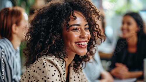 A woman with curly hair smiles confidently while interacting with coworkers at a business meeting. 