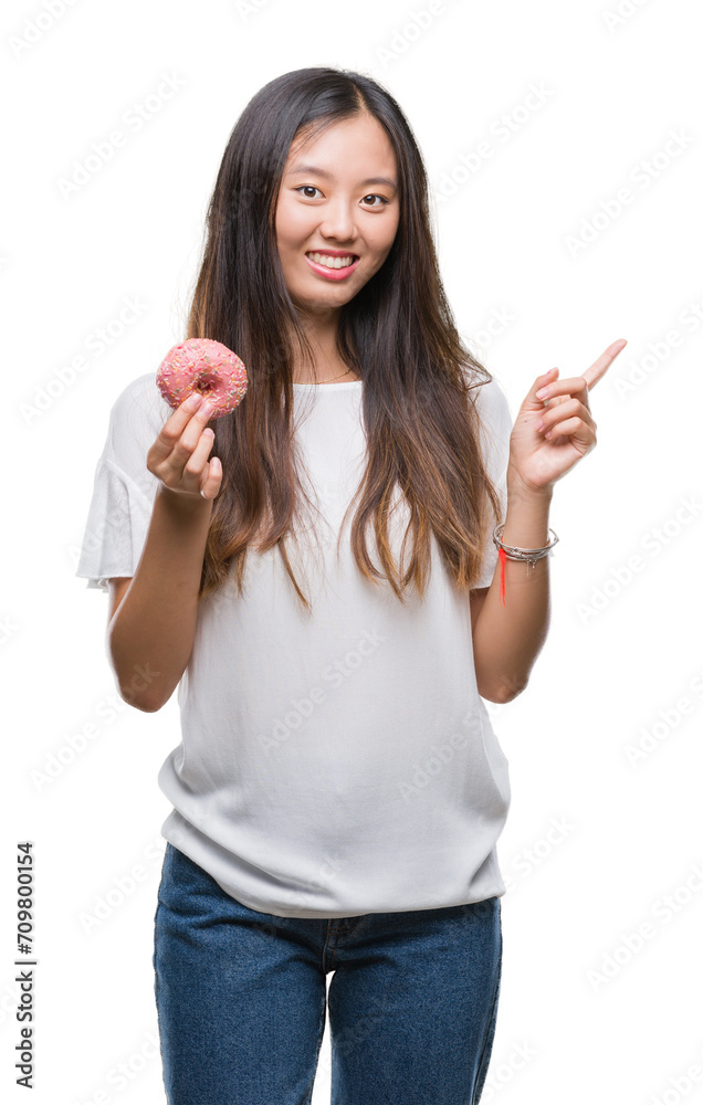 Young asian woman eating donut over isolated background very happy pointing with hand and finger to the side Young asian woman eating donut over isolated background very happy pointing with hand and finger to the side