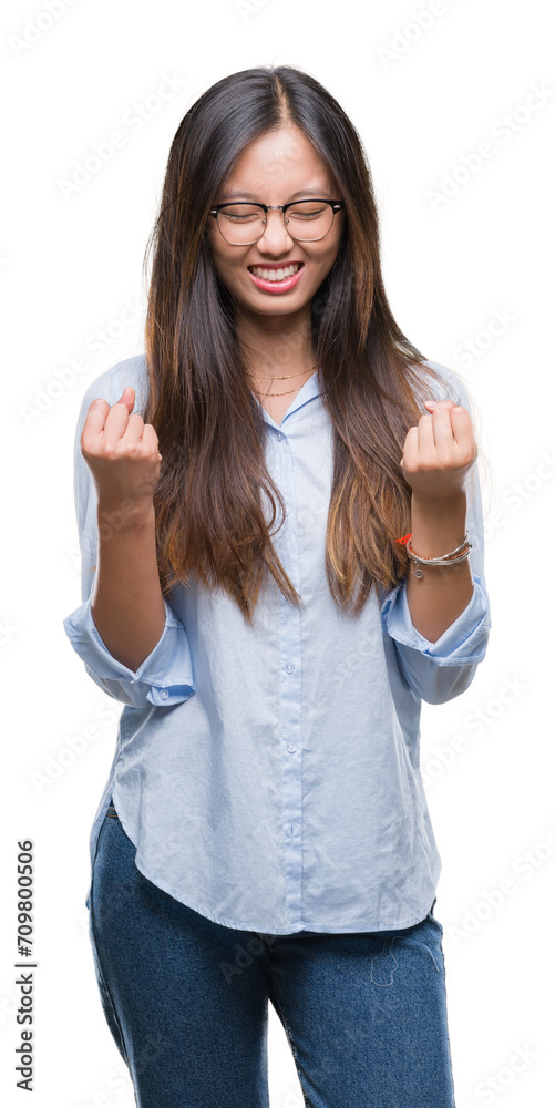 Young asian business woman wearing glasses over isolated background very happy and excited doing winner gesture with arms raised, smiling and screaming for success. Celebration concept. Young asian business woman wearing glasses over isolated background very happy and excited doing winner gesture with arms raised, smiling and screaming for success. Celebration concept.
