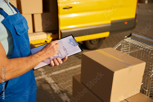 Professional male courier filling out delivery form on postal parcels photo
