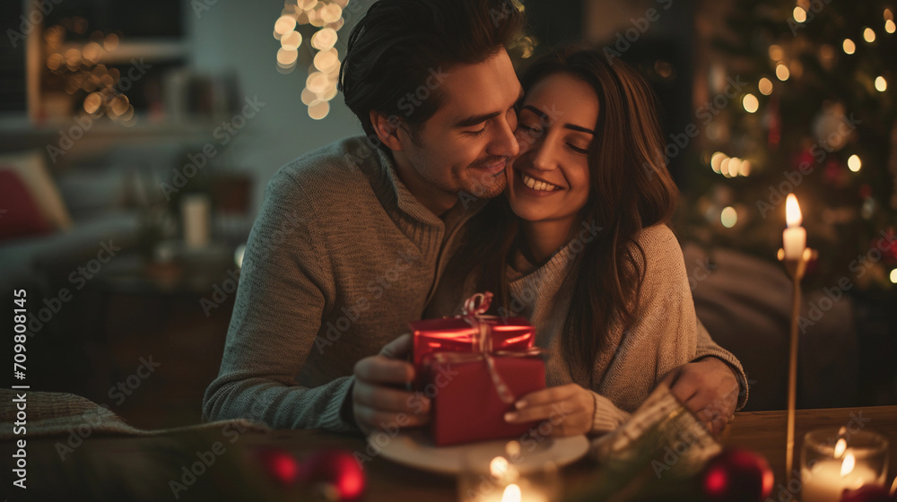 Young Couple Celebrating Anniversary or Valentine's Day with Romantic Dinner at Home. Man Giving Red Gift Box, Hugging Woman, Making Present Surprise in Candlelight Young Couple Celebrating Anniversary or Valentine's Day with Romantic Dinner at Home. Man Giving Red Gift Box, Hugging Woman, Making Present Surprise in Candlelight