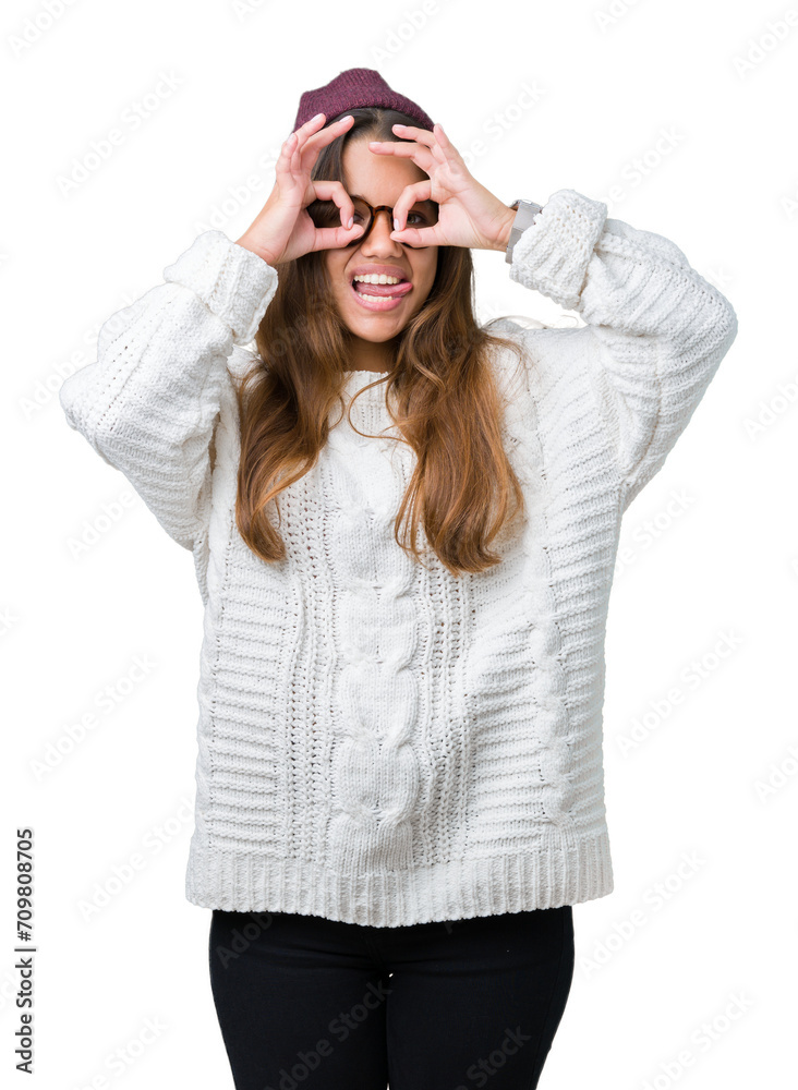 Young beautiful brunette hipster woman wearing glasses and winter hat over isolated background doing ok gesture like binoculars sticking tongue out, eyes looking through fingers. Crazy expression. Young beautiful brunette hipster woman wearing glasses and winter hat over isolated background doing ok gesture like binoculars sticking tongue out, eyes looking through fingers. Crazy expression.