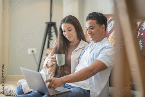 Young couple moving to a new home relaxing sitting on the sofa using computer laptop, smiling happy for moving to new apartment