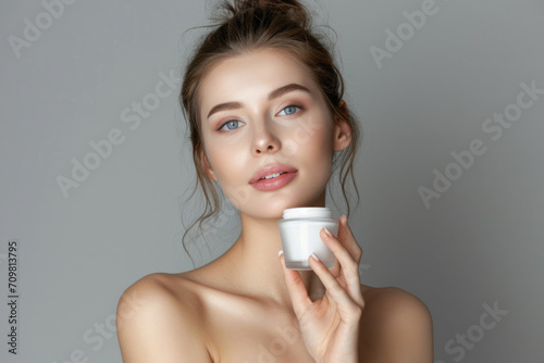 Beautiful young woman with clean fresh skin holding a jar of cream.