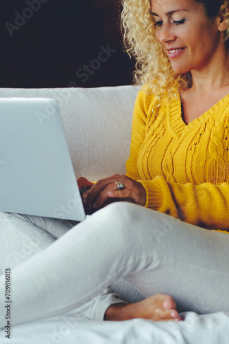 One woman at home sitting on the sofa surfing the web and using laptop in leisure technology connection activity. Modern female people writing on computer alone comfortably on the couch and smile