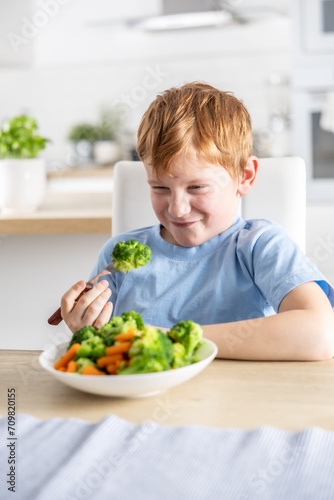 The little boy looks with distaste at the broccoli on his fork