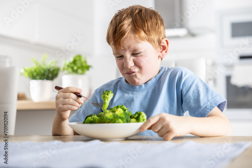 The little boy looks with distaste at the broccoli on his fork