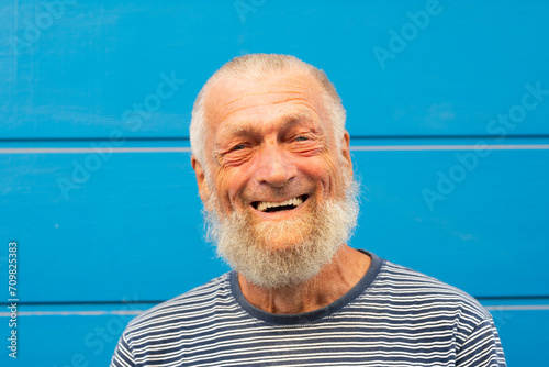75 year old senior man laughs while having a good time outdoors. Portrait with blue background. Leisure and people concept