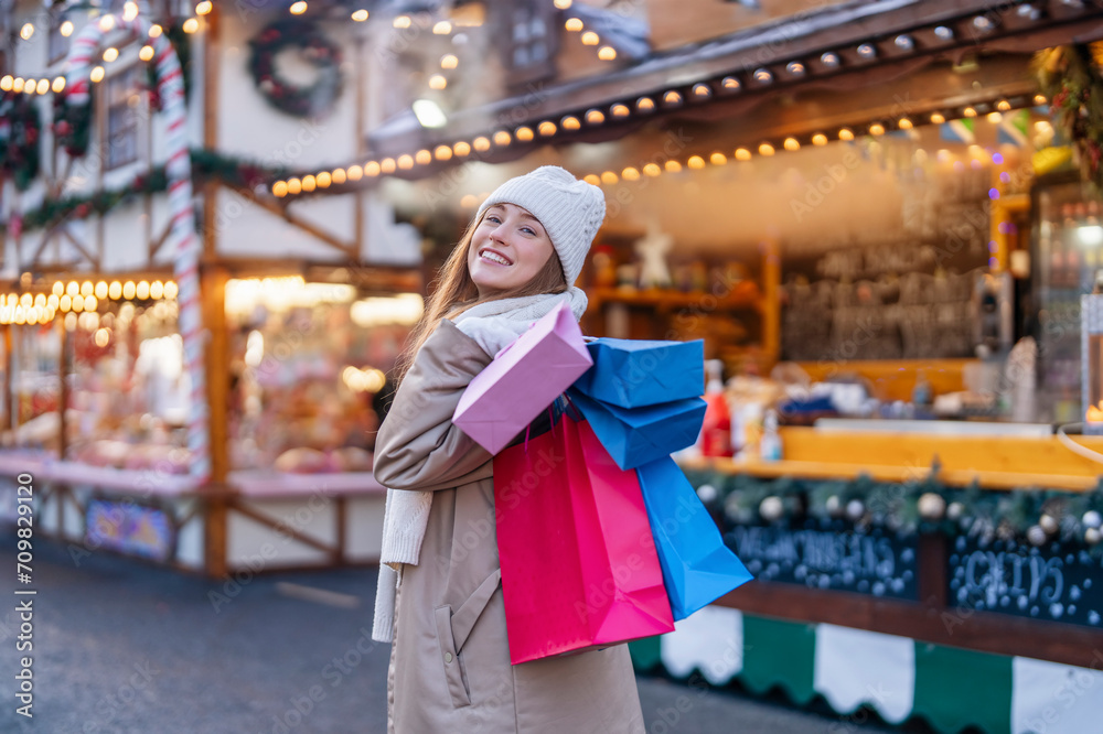 smiling young woman with colorful shopping gift bags  having a fun time,  using phones,   outdoor in an urban winter city. people, communication,  shopping and lifestyle concept