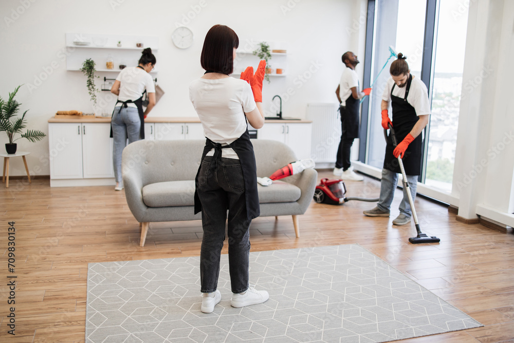 Fototapeta premium Female boss of company distributes tasks to employees and points to cleaning locations. Professional housekeeper services company team working at customer house washing dishes, kitchen cleaning.