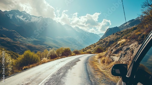 A car cruises through mountainous terrain and on a winding road.