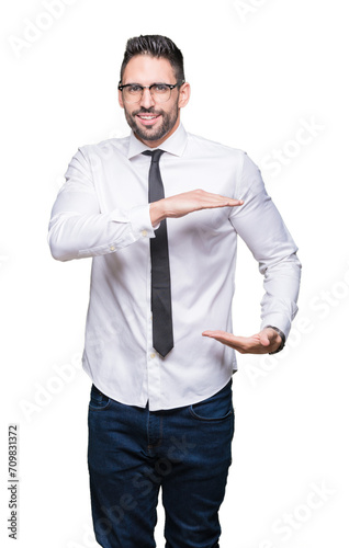 Young handsome business man wearing glasses over isolated background gesturing with hands showing big and large size sign, measure symbol. Smiling looking at the camera. Measuring concept.