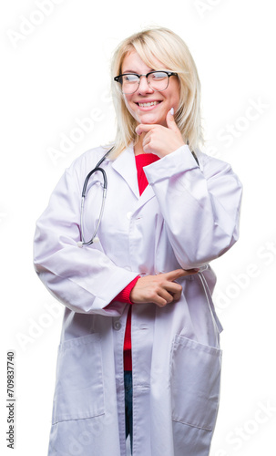 Young beautiful blonde doctor woman wearing medical uniform over isolated background looking confident at the camera with smile with crossed arms and hand raised on chin. Thinking positive.