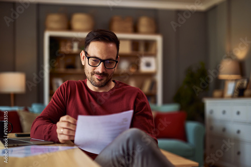 Canvastavla A content male writer revising his work on a paper that he is holding while sitting in his home office