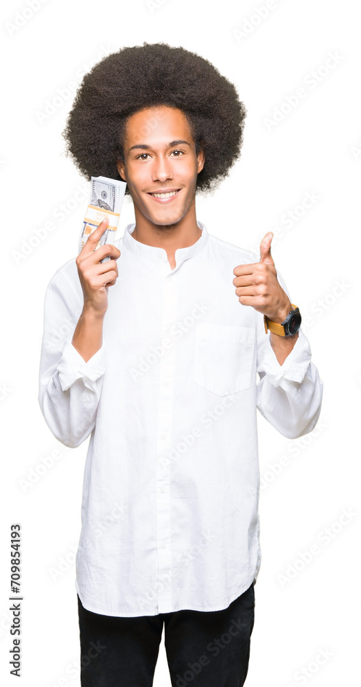 Young african american man with afro hair holding bunch of dollars happy with big smile doing ok sign, thumb up with fingers, excellent sign