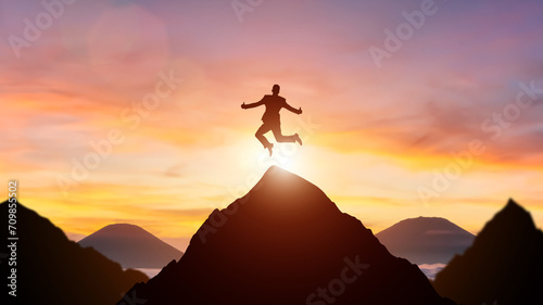 Silhouette of a person leaping between mountain peaks against a vibrant sunset sky. photo