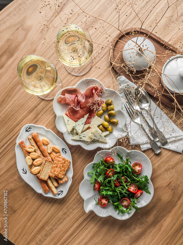 Aperitif, tapas, appetizer arugula table, cherry salad, plate with prosciutto, olives, cheese and breadsticks, cracker on a wooden background, top view