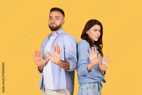 Couple gesturing stop with hands, standoffish poses, yellow background