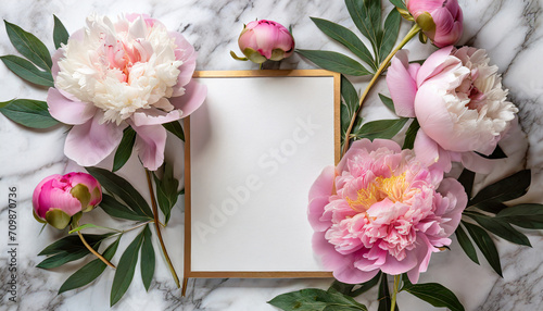 Blank greeting card in frame made of pink peony flowers on white marble background. Wedding invitation. Mock up. Flat lay photo