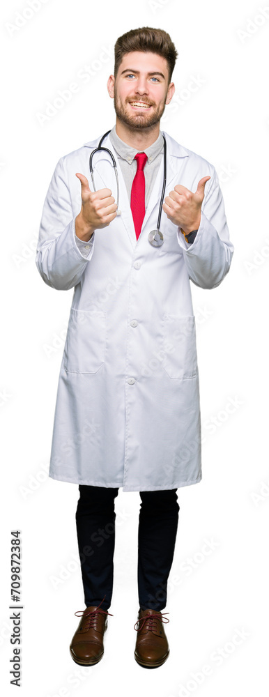 Young handsome doctor man wearing medical coat success sign doing positive gesture with hand, thumbs up smiling and happy. Looking at the camera with cheerful expression, winner gesture. Young handsome doctor man wearing medical coat success sign doing positive gesture with hand, thumbs up smiling and happy. Looking at the camera with cheerful expression, winner gesture.