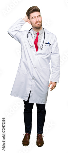Young handsome doctor man wearing medical coat confuse and wonder about question. Uncertain with doubt, thinking with hand on head. Pensive concept.