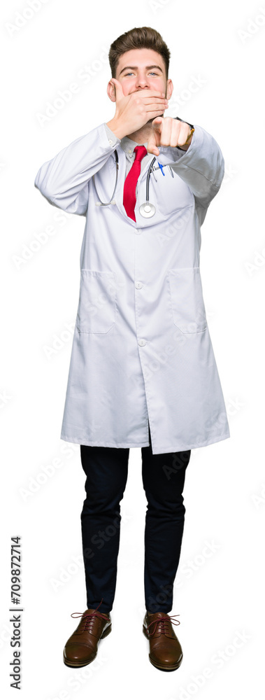 Young handsome doctor man wearing medical coat Laughing of you, pointing to the camera with finger hand over mouth, shame expression Young handsome doctor man wearing medical coat Laughing of you, pointing to the camera with finger hand over mouth, shame expression